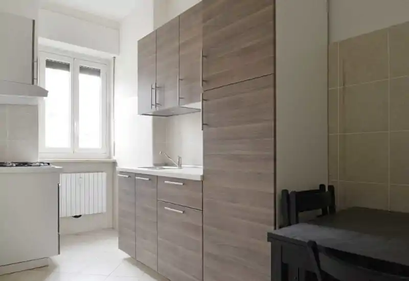 Cuisine compacte et lumineuse avec meubles effet bois, évier sous des placards muraux et fenêtre apportant de la lumière naturelle — pratique et soignée pour un petit appartement.