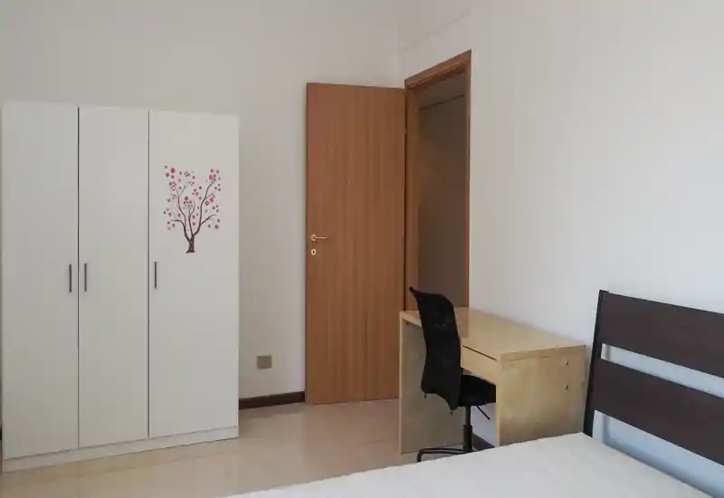 Chambre lumineuse et sobre avec lit visible, armoire blanche et bureau en bois — parfaite pour une personne seule ou un étudiant.