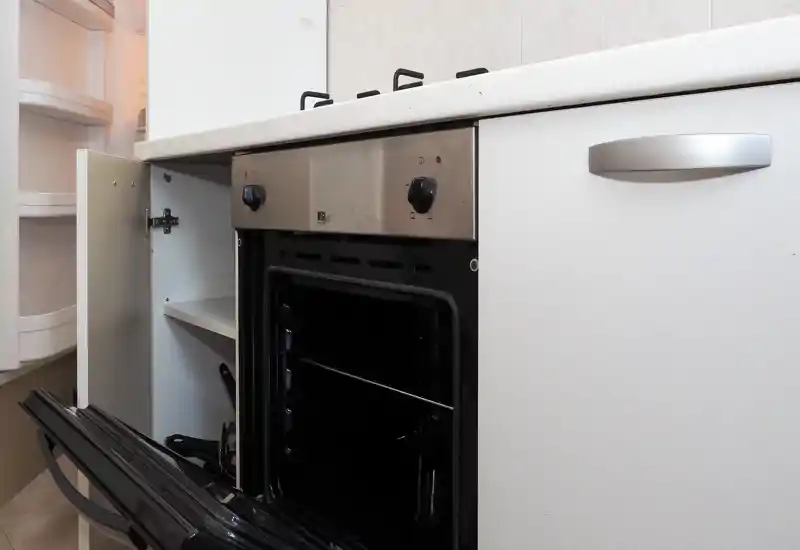 Gros plan d'une petite cuisine montrant une porte de four ouverte, les boutons de la plaque et des placards — un espace de cuisson fonctionnel.