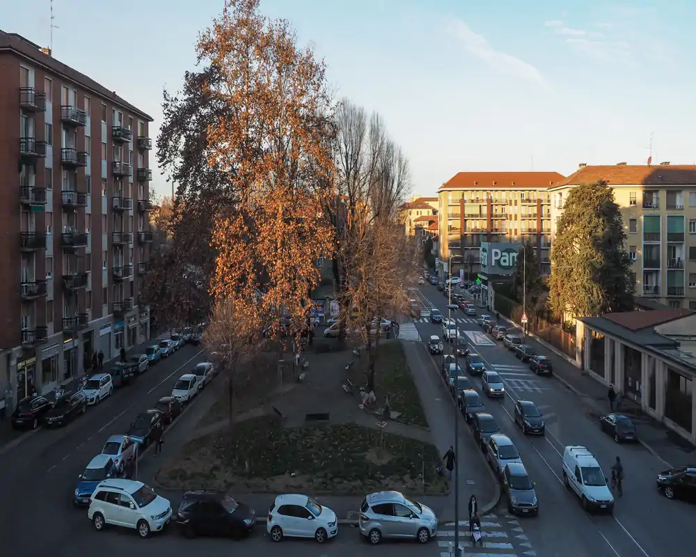 Urban outdoor view from a higher floor showing a tree-lined traffic island, surrounding streets and apartment buildings — ideal to convey location and street atmosphere.