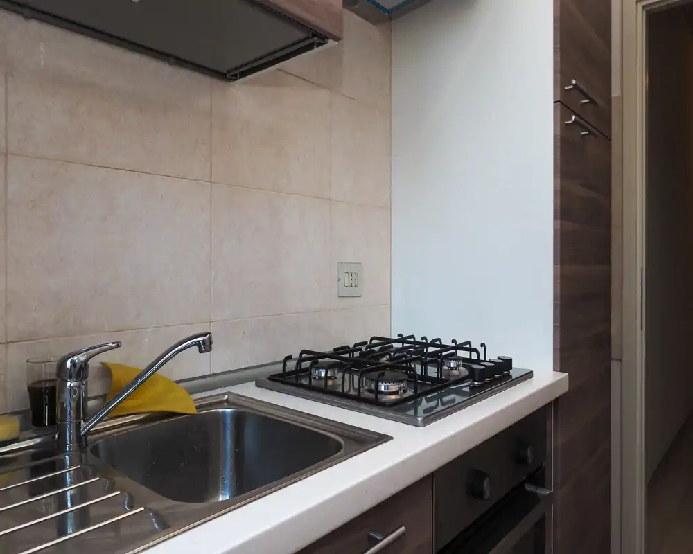 Compact modern kitchen corner with a stainless sink, gas hob and wood-effect cabinets — clean surfaces and neutral tile backsplash.