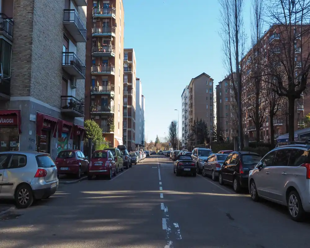 Sunny urban street view with parked cars and residential buildings on both sides, useful for showing the neighborhood and immediate surroundings.