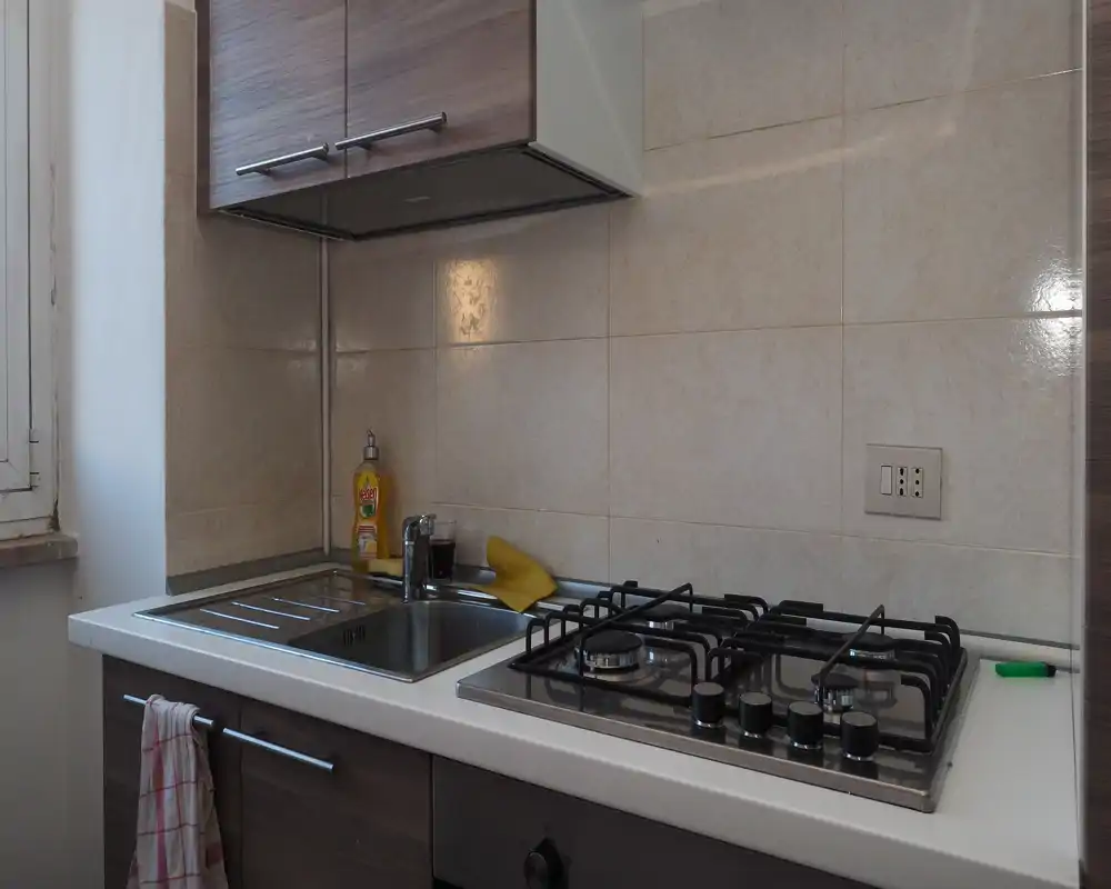 Compact, modern kitchen corner with a gas hob, stainless sink and wall cabinets. Bright natural light from the window and tidy surfaces make it suitable for short-term rentals.