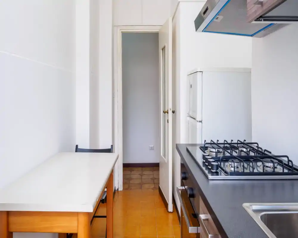 Cocina compacta y moderna con encimera de gas, horno y pequeño frigorífico; superficies limpias y mesa sencilla, ideal para un piso urbano.