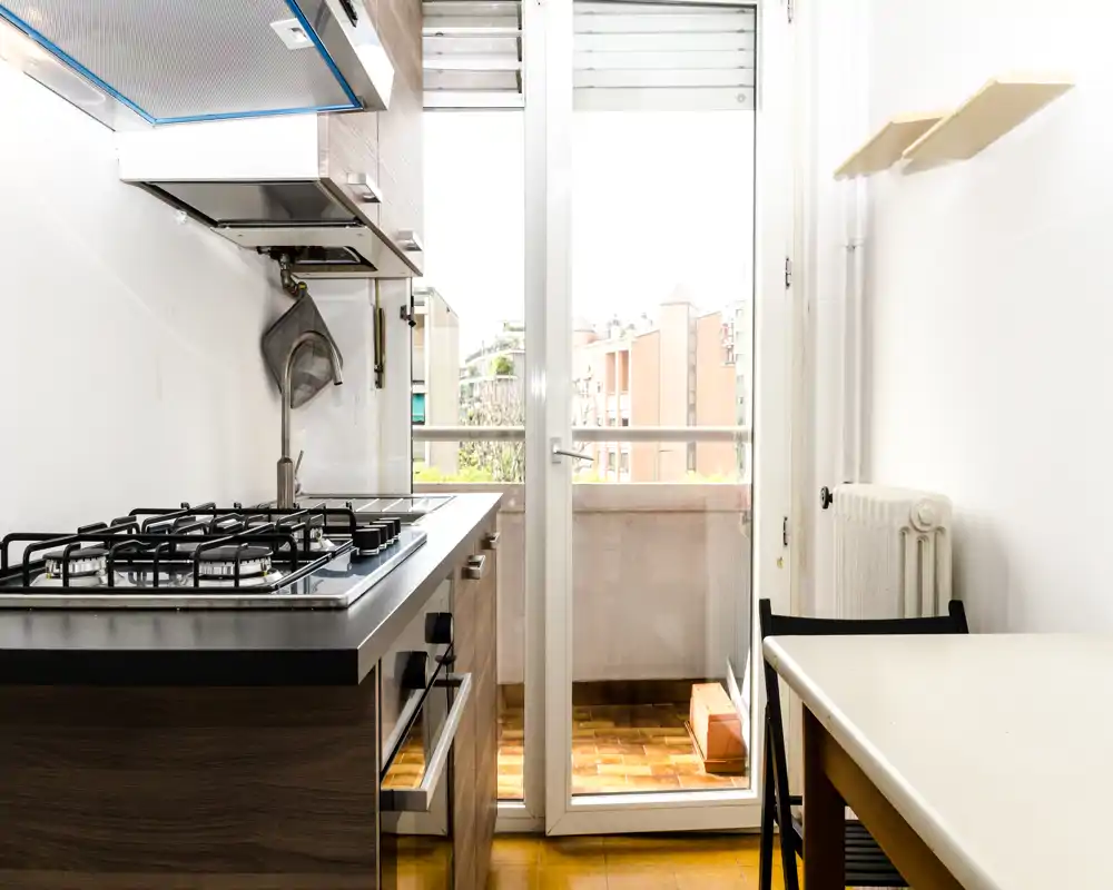 Cocina moderna y compacta con placa de gas, campana extractora y acceso directo a un pequeño balcón — diseño luminoso y funcional, ideal para apartamentos en la ciudad.