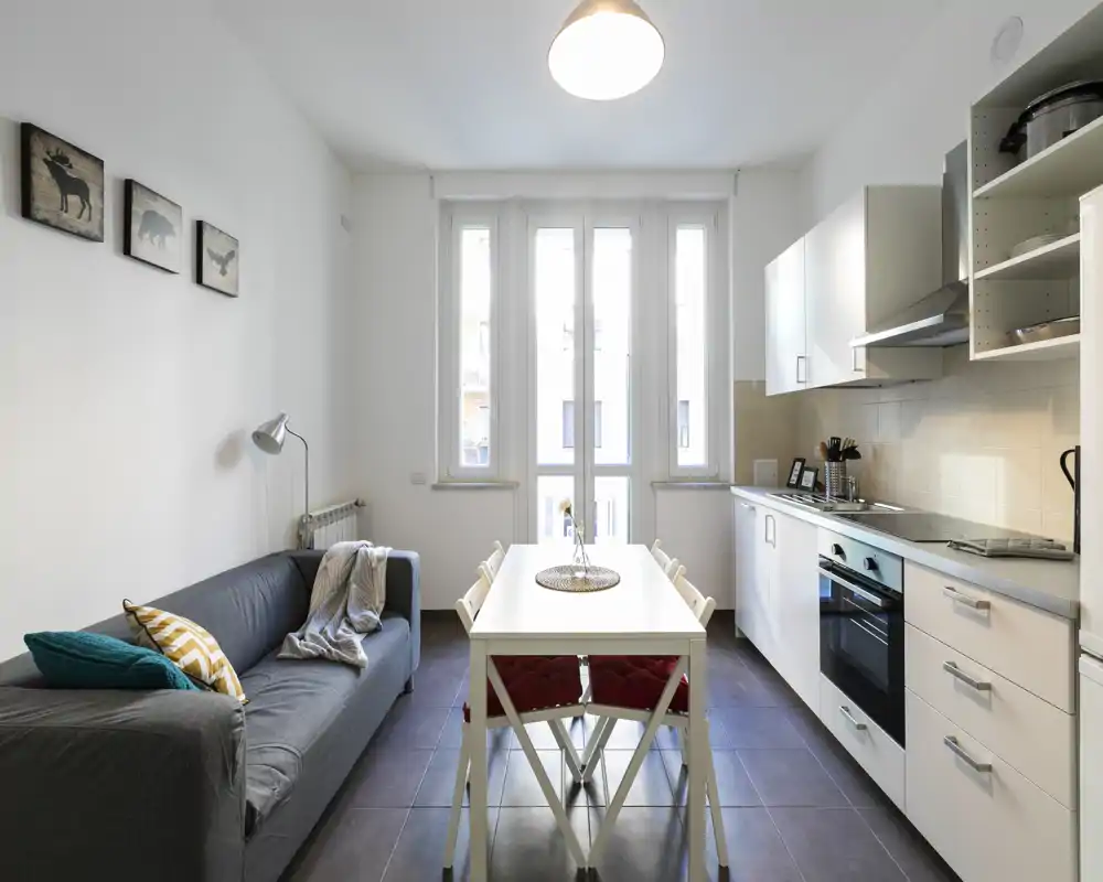 Zona de día moderna y luminosa tipo open-plan con cocina equipada, mesa para cuatro y un sofá cómodo — ideal para alquileres urbanos que buscan funcionalidad y estilo.