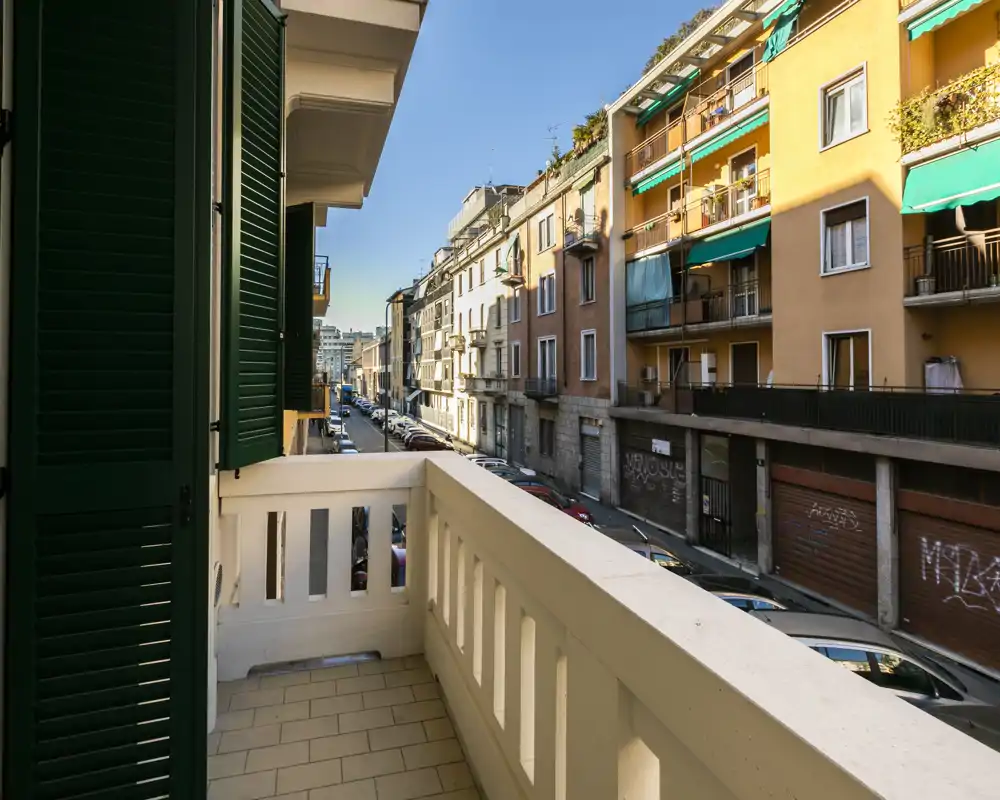 Balcón soleado con vistas a una tranquila calle urbana y edificios clásicos con persianas verdes — perfecto para el café de la mañana.
