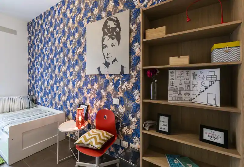 Dormitorio compacto y con estilo, con pared decorativa, cama individual con ropa de cama, mesita con lámpara y estantería abierta — luminoso, bien decorado y acogedor para una persona.