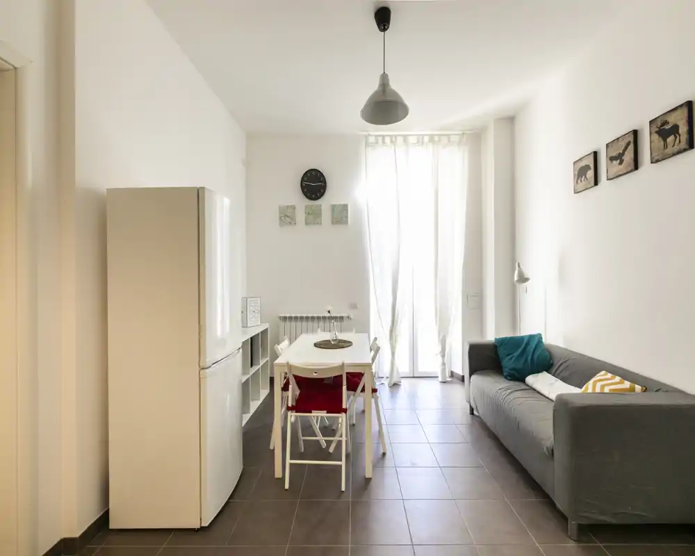 Área de estar moderna y luminosa con mesa de comedor compacta, sofá cómodo y una gran puerta acristalada que aporta luz natural.