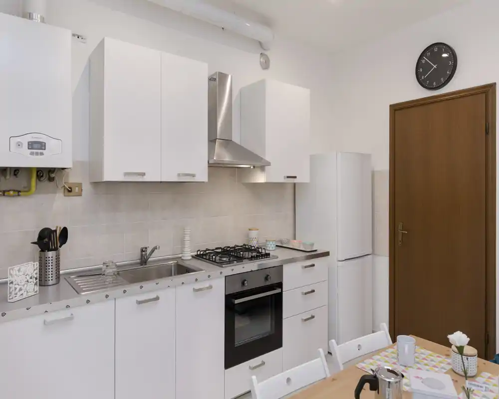 Cocina moderna y luminosa con muebles blancos, placa de gas, horno y pequeña mesa — ordenada y bien iluminada, ideal para estancias cortas.