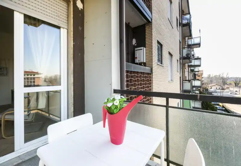 Balcone privato soleggiato con tavolo e sedie e una vivace pianta in vaso — ideale per caffè mattutino e relax all'aperto.