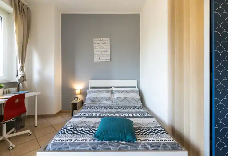 Dormitorio luminoso y bien decorado con ropa de cama estampada, lámpara de noche y pequeño escritorio junto a la ventana — ideal para una estancia cómoda.