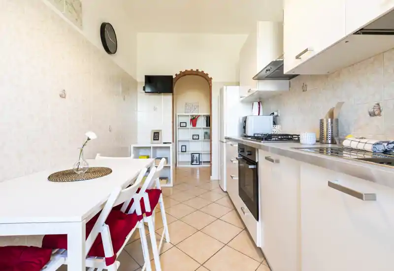 Cucina luminosa e moderna con piano di lavoro completo, forno incassato, piano cottura e tavolo da pranzo con sedie con cuscini rossi—ben attrezzata e ordinata per pasti confortevoli.