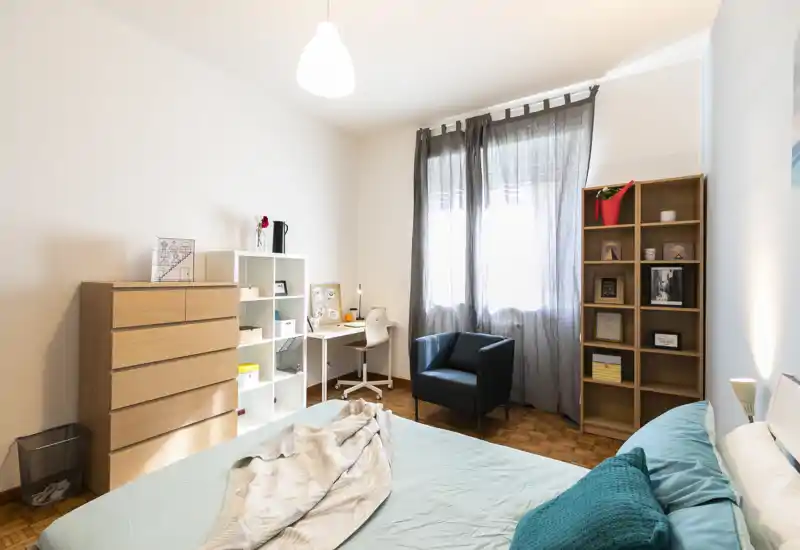 Dormitorio luminoso y bien decorado con cama doble en primer plano, sillón y escritorio junto a la ventana — ideal para una estancia cómoda.
