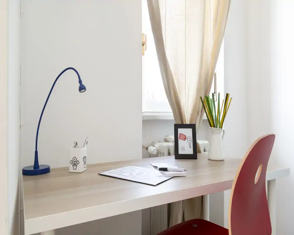 Bright, minimal desk area with a simple wooden tabletop, blue task lamp and a red chair — ideal for a compact home office or study nook.