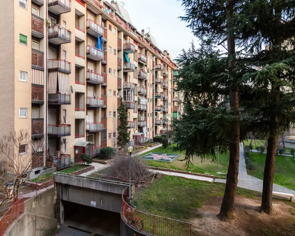Communal courtyard view with landscaped green areas, mature trees and building balconies surrounding the garden — a bright exterior space suitable for relaxing.
