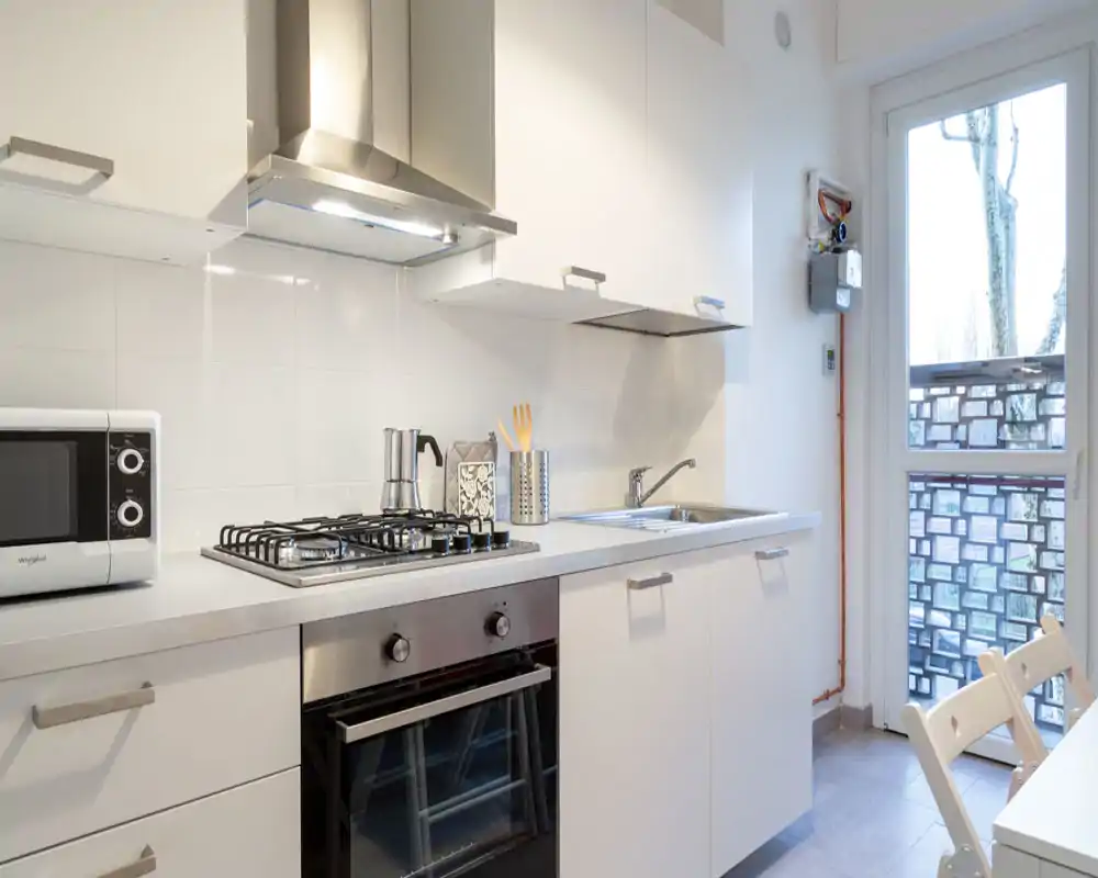 Bright modern kitchen with gas hob, built-in oven, stainless-steel sink and white cabinets; compact, clean layout ideal for small apartments.