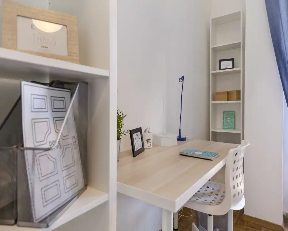 Bright, minimal study corner with a wooden desk, white shelving and a perforated chair — ideal for a compact home office.