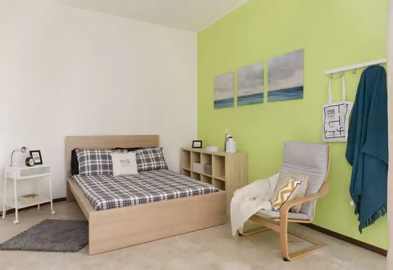 Bright, neatly staged bedroom with a wooden double bed, patterned bedding and cozy armchair beside a lime-green accent wall.
