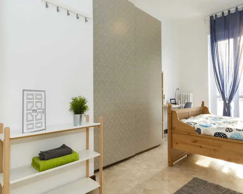 Chambre lumineuse et bien agencée avec un lit simple en bois, une literie à motifs et une grande fenêtre apportant une belle lumière naturelle.