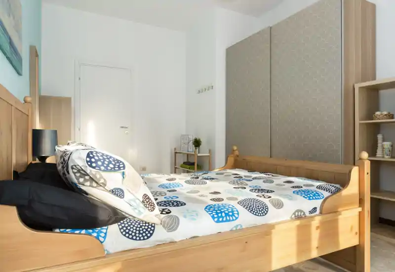 Camera da letto luminosa e ben arredata con letto in legno, biancheria a fantasia e un ampio armadio; la luce naturale rende l'ambiente arioso e accogliente.