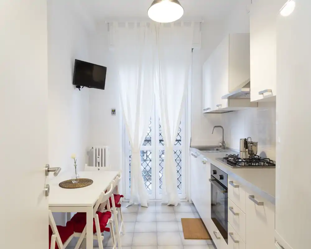Cucina moderna e luminosa con elettrodomestici integrati, piano cottura a gas e un piccolo tavolo da pranzo vicino alla finestra con tende leggere — perfetta per soggiorni in città.