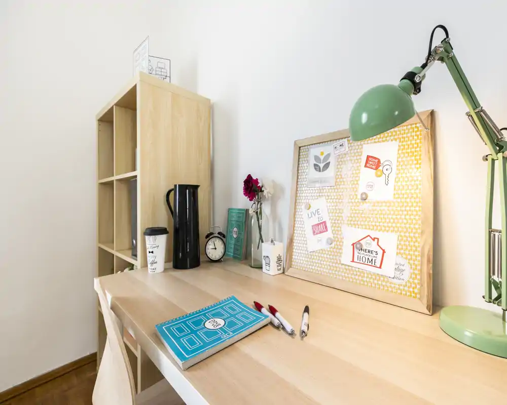 Bright, tidy desk corner with a wooden table, chair, bulletin board with notes, desk lamp and small decorative items — ideal for a cozy home office or study nook.
