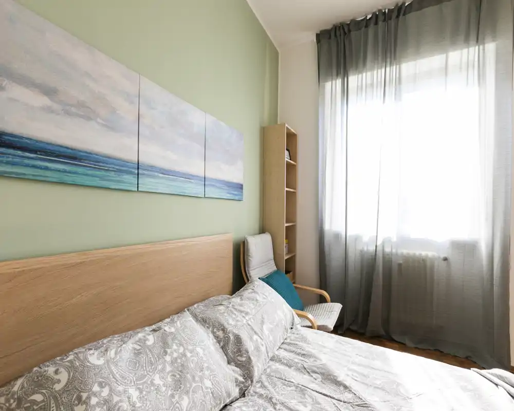 Bright, well-styled bedroom with a wooden headboard, patterned bedding and a large window that fills the room with natural light.