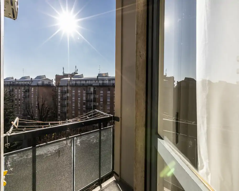 Sunny private balcony with metal railing, partial view of neighboring buildings and clear blue sky—ideal for morning coffee.
