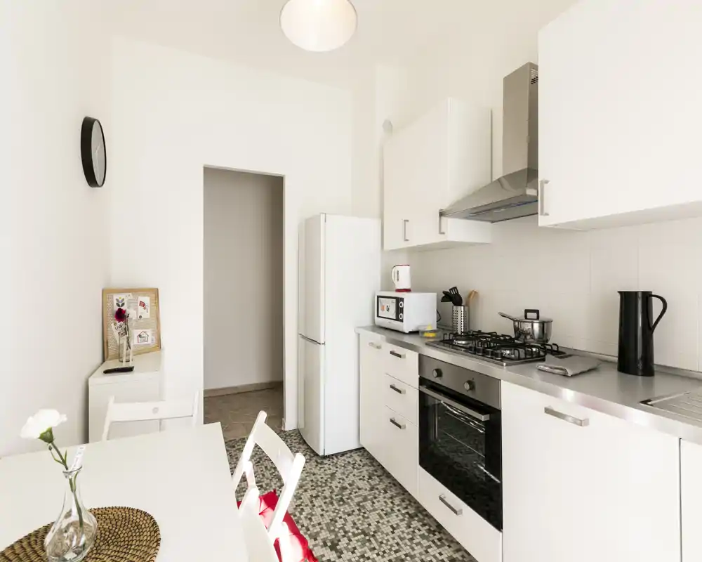 Bright modern kitchen with white cabinets, gas stove, oven and a compact dining table. Clean, well-lit space with simple decorative touches (vase, placemat) ideal for short-term rentals.