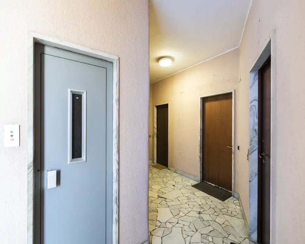 Shared building entrance/hallway with multiple apartment doors, tiled floor and soft overhead lighting — clean and well lit common corridor.