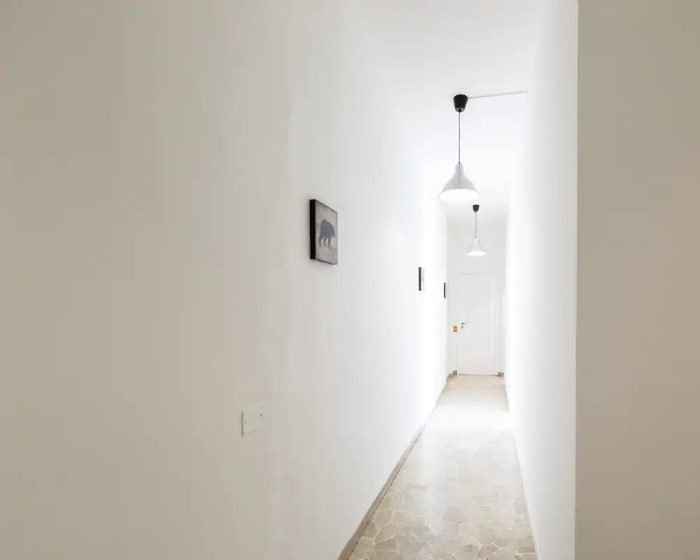 Bright, narrow entrance hallway with white walls, pendant lights and tiled floor leading to an interior door — clean and minimal circulation space.