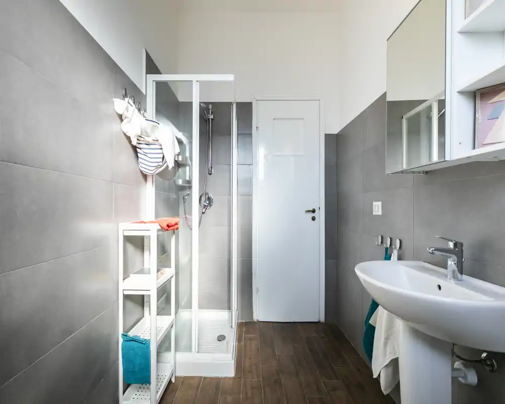 Bright, modern bathroom with a glass shower enclosure, pedestal sink, wall-mounted mirror cabinet and wood-effect floor tiles.