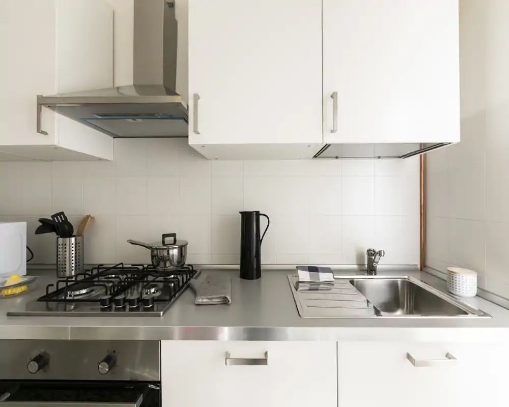 Clean, modern kitchenette with stainless-steel countertop, gas hob and sink. Minimal styling with practical utensils and good natural light.