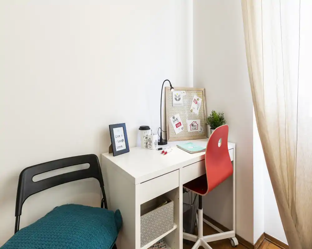 Coin bureau lumineux et soigné avec un bureau blanc, une chaise pivot rouge, un panneau d'affichage décoratif et une douce lumière naturelle — idéal pour travailler ou étudier.