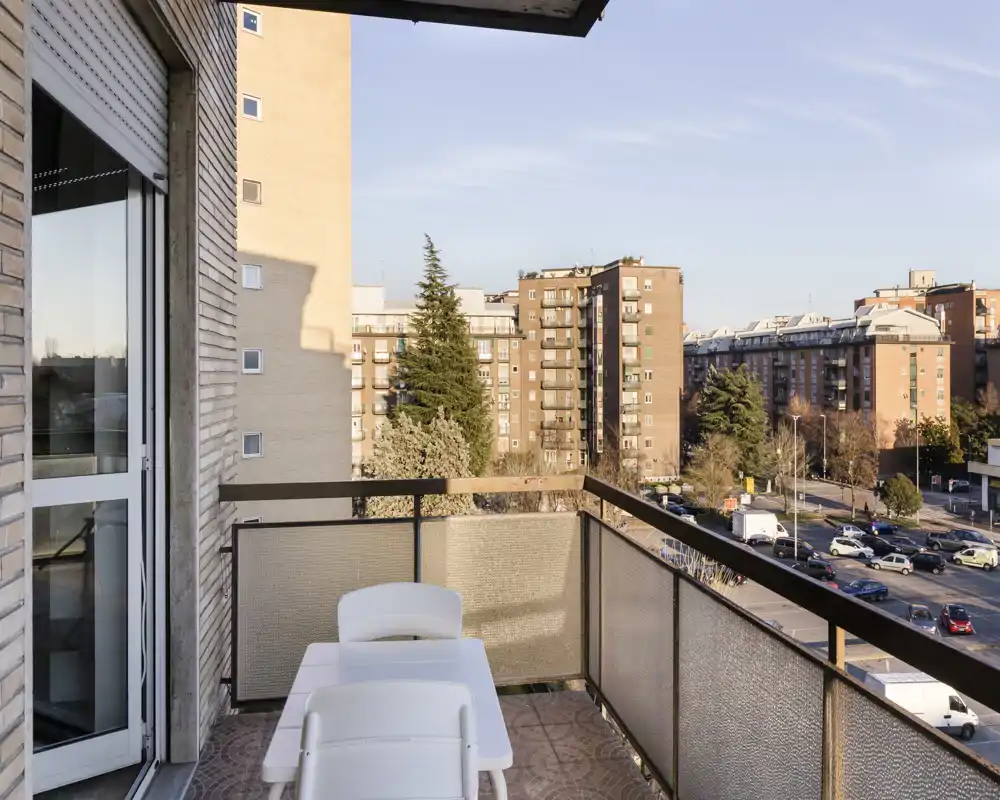 Balcón soleado con mesa y sillas, con vistas a un barrio residencial y aparcamientos — ideal para tomar un café por la mañana o relajarse al aire libre.
