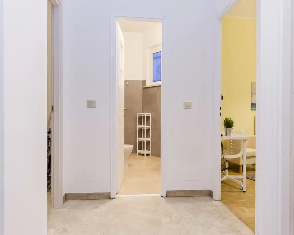 Entrada/pasillo luminoso y neutro con tres puertas que conducen a habitaciones contiguas, suelo en baldosa y paredes blancas limpias.