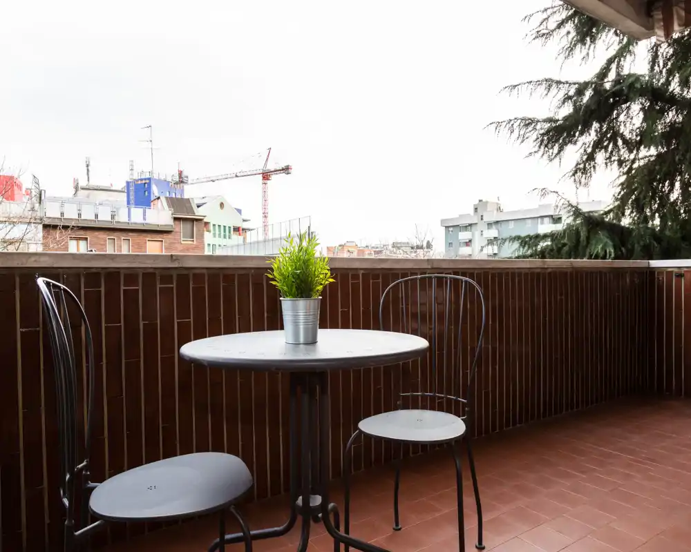 Balcone soleggiato con un piccolo tavolo rotondo, due sedie in metallo e una pianta in vaso — ideale per il caffè mattutino con vista sulla città.