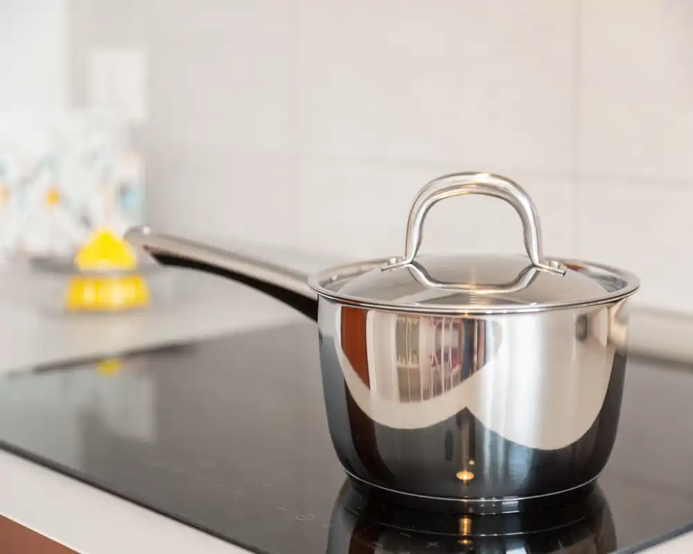 Plano detalle de una cacerola de acero inoxidable sobre una placa de inducción moderna, con superficies limpias y luz natural suave.