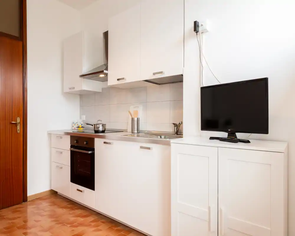 Cocina compacta y moderna con armarios blancos, horno integrado, fregadero y encimera. Luminosa y limpia, adecuada para alquileres temporales o estudios.