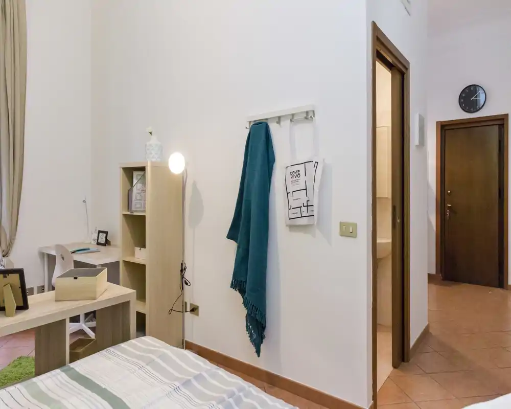 Dormitorio luminoso y ordenado con cama visible, lámpara, estantería y pequeño espacio de escritorio — acogedor y bien decorado para alquileres temporales.