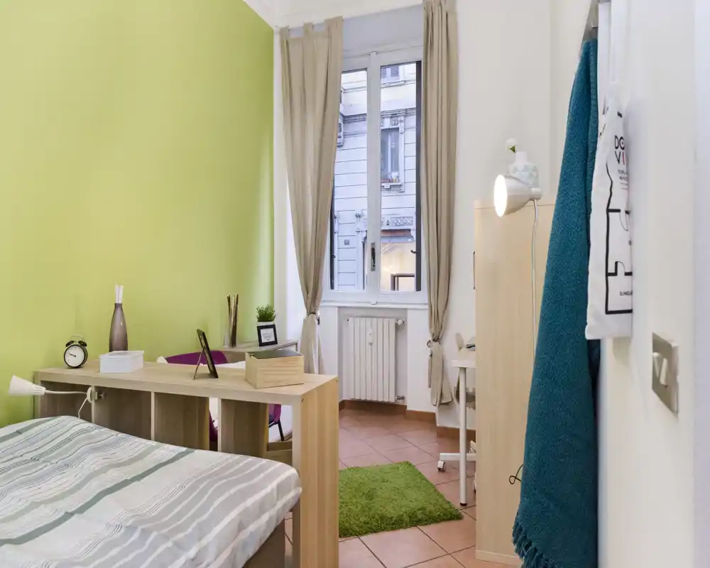 Dormitorio luminoso y ordenado con cama individual, amplia ventana que aporta luz natural, muebles de madera clara y textiles suaves que crean un ambiente acogedor.