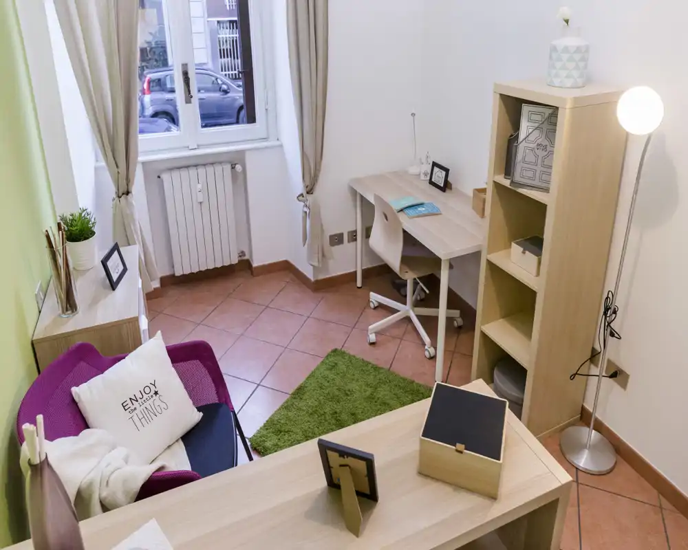 Zona de estar luminosa y bien preparada con un sillón acogedor, cojines decorativos y un pequeño escritorio — ideal para relajarse o trabajar junto a la ventana.