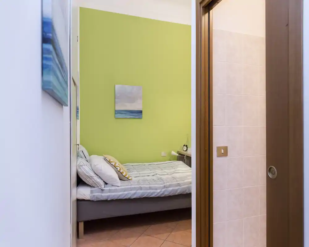 Dormitorio compacto y bien decorado con cama individual, mesilla y pared verde en tonos relajantes — luminoso y acogedor para estancias cortas.