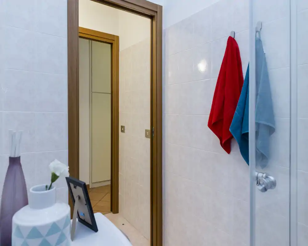 Baño pequeño y limpio con paredes alicatadas, toallas colgadas, puerta de ducha de cristal y artículos decorativos sobre el lavabo.