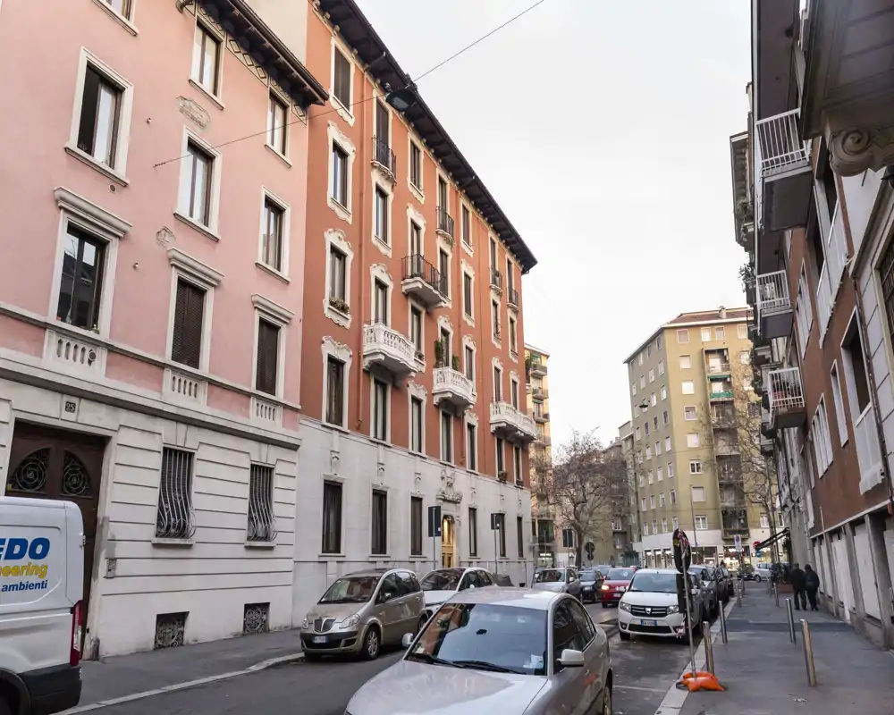Exterior a la calle con edificios residenciales de altura media, coches aparcados y un ambiente urbano tranquilo — ideal para mostrar la fachada y el vecindario.