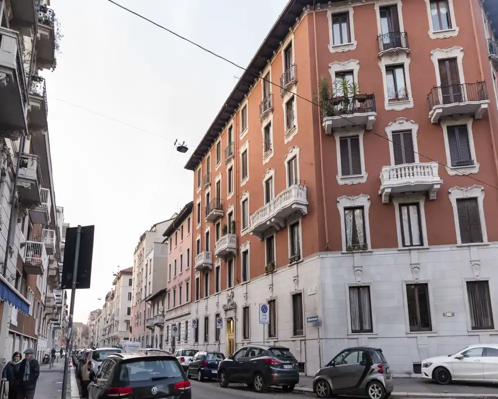 Foto a nivel de calle de una fachada residencial con coches aparcados, que muestra detalles arquitectónicos y balcones.