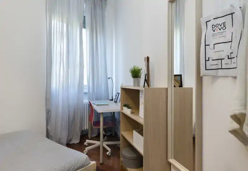 Piccola camera da letto luminosa con letto singolo, scrivania e scaffalatura — ordinata, moderna e ideale per studenti o soggiorni brevi.