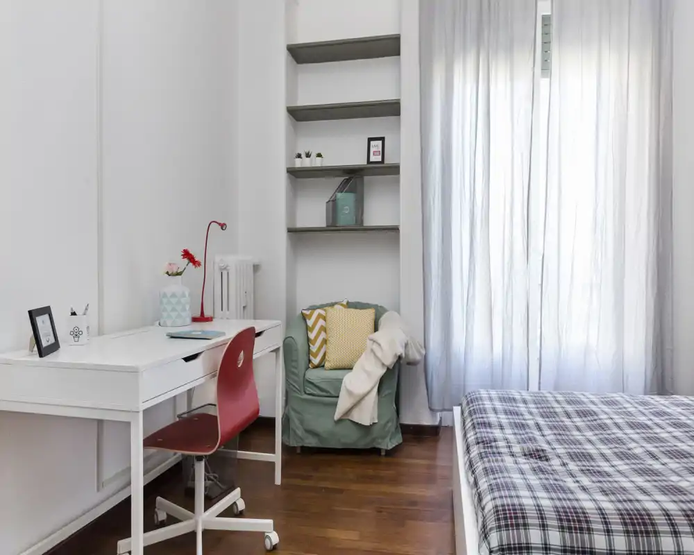 Dormitorio luminoso y bien decorado con cama cómoda, escritorio y un sillón acogedor junto a la ventana que aporta luz natural.