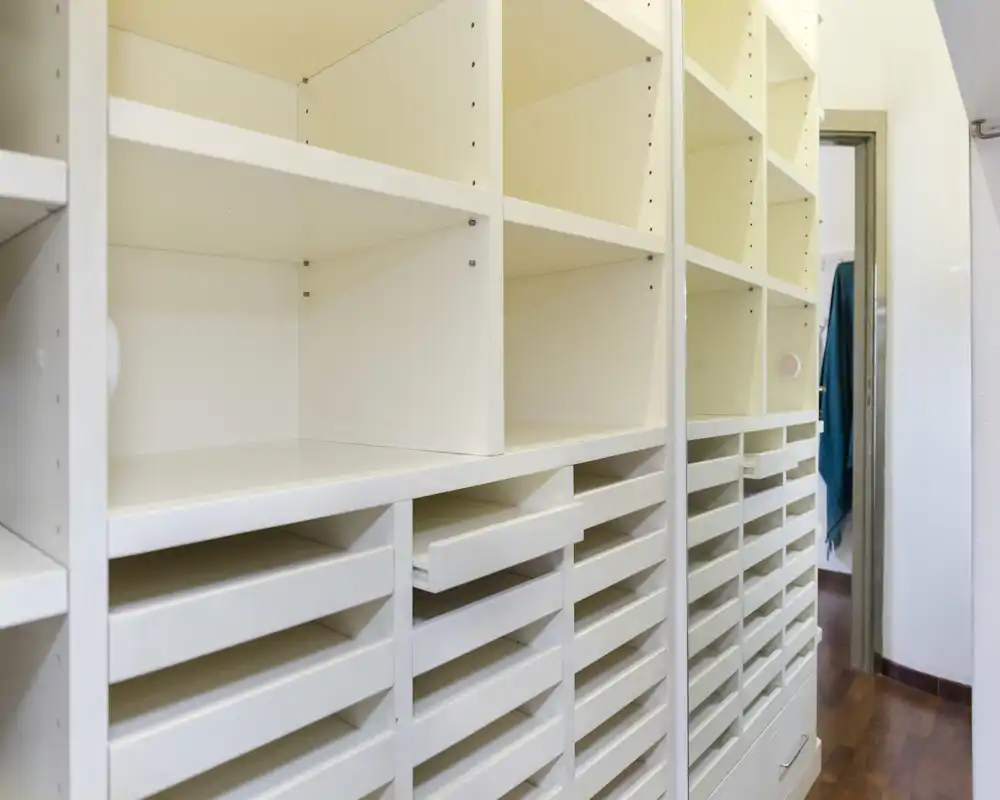 Estanterías blancas empotradas y múltiples cajones poco profundos en una entrada estrecha o vestidor, ideal para almacenamiento organizado.